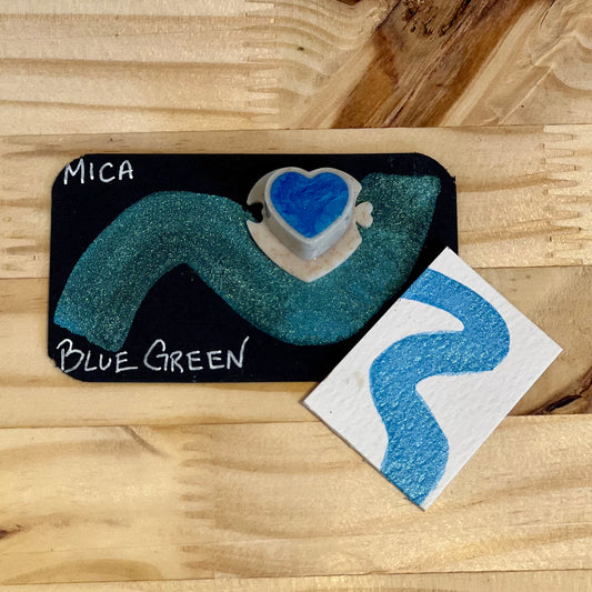 blue green mica shimmer watercolor paint  heart shape paint pan with swatch on on a black card with 'Mica Blue Green' text and small swatch on white paper