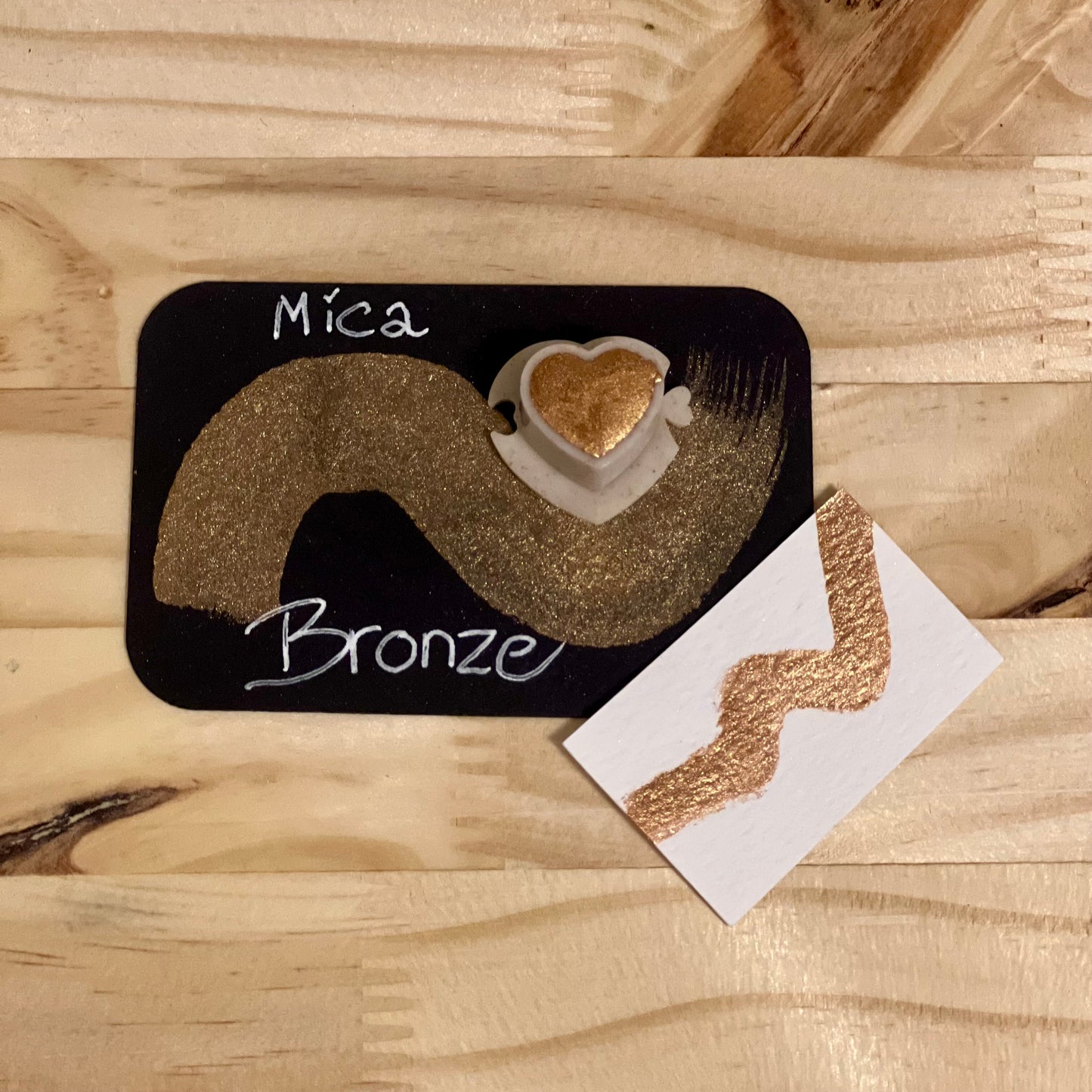 bronze mica shimmer watercolor paint in  heart shape paint pan with swatch on on a black card with 'Mica Bronze' text and small swatch on white paper