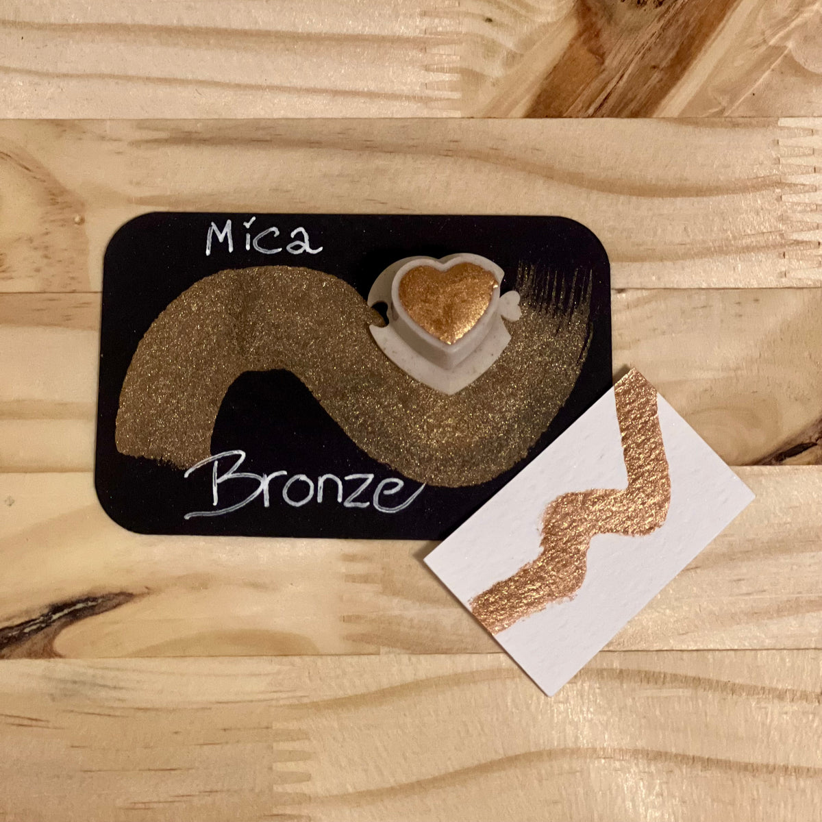 bronze mica shimmer watercolor paint in  heart shape paint pan with swatch on on a black card with 'Mica Bronze' text and small swatch on white paper