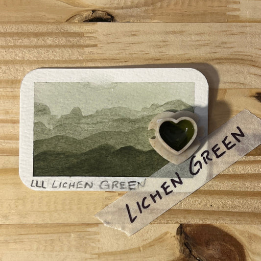 Card with landscape illustration and heart-shaped pan on a wooden surface with 'Lichen Green' label text.