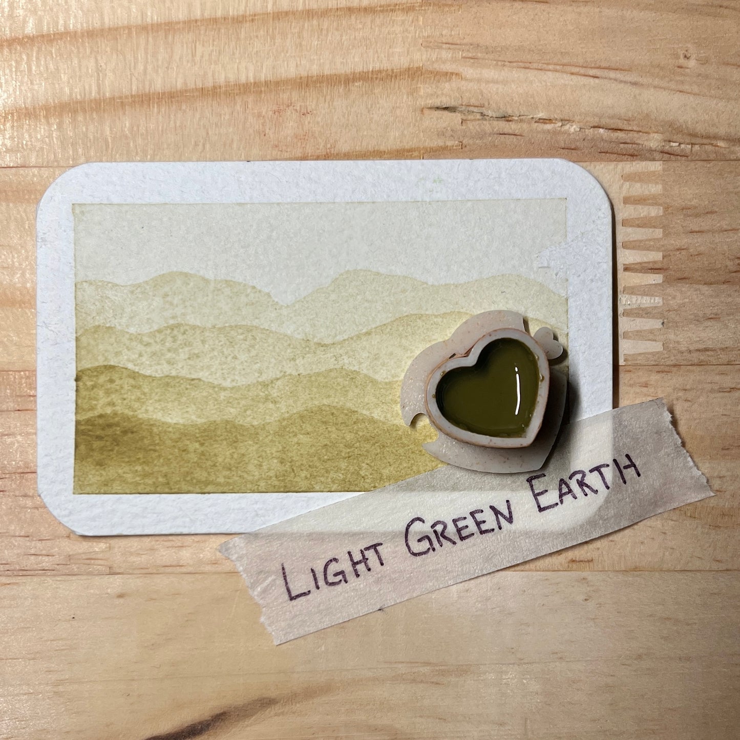Light Green watercolor gradient landscape, heart-shape watercolor pan, labeled 'Light Green Earth', on a wooden surface.