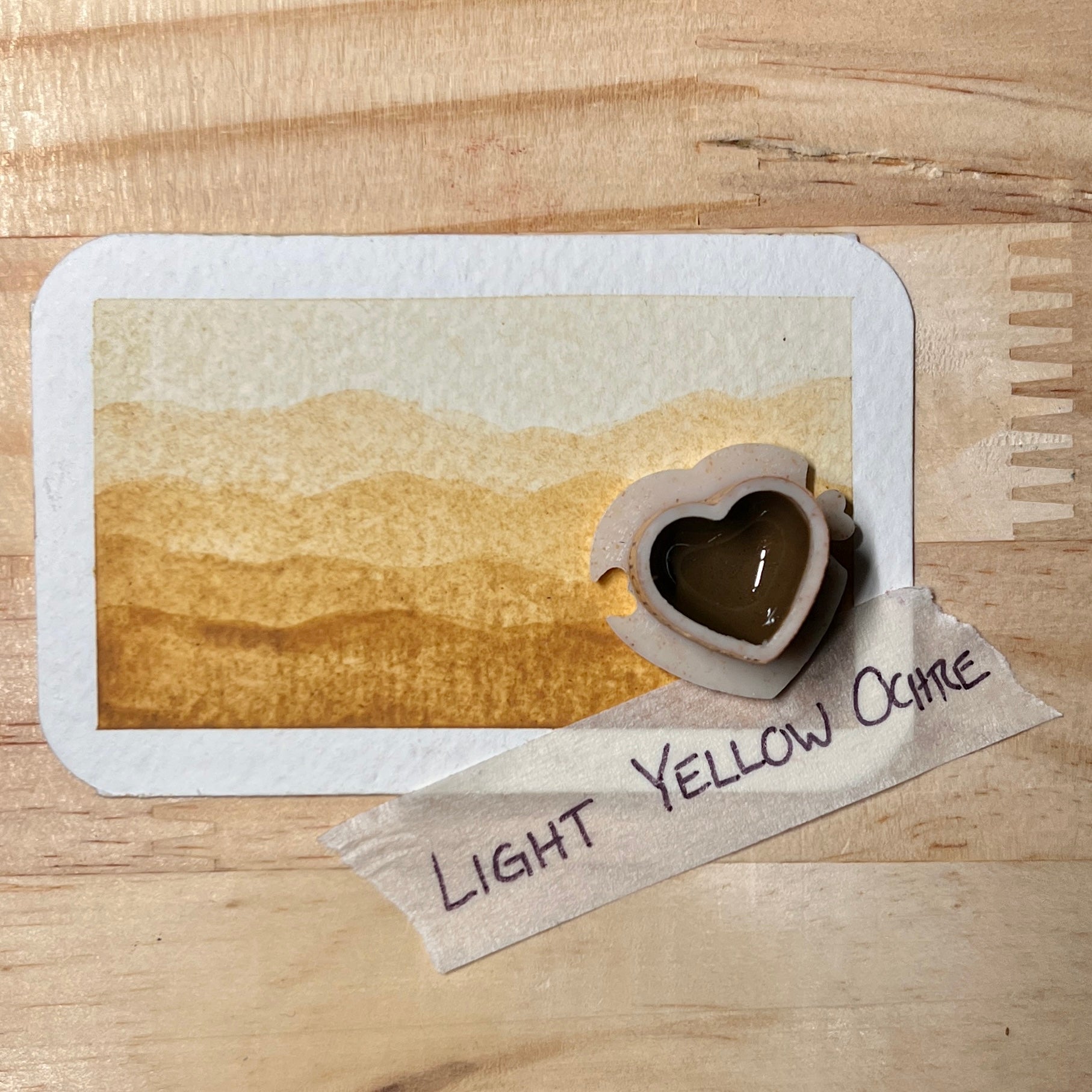 Light yellow watercolor gradient landscape, heart-shape watercolor pan, labeled 'Light Yellow Ochre', on a wooden surface.
