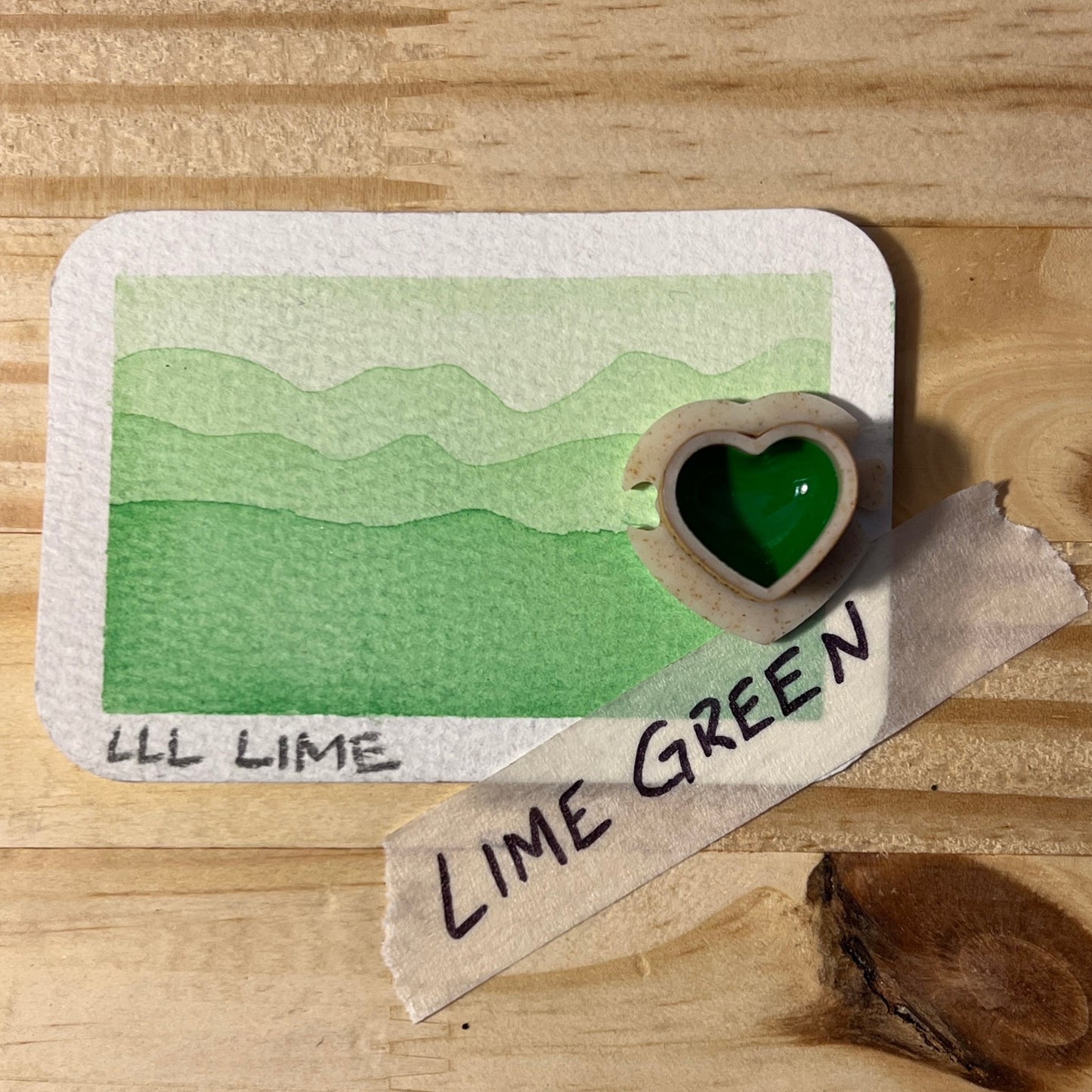 Lime green color swatch on a wooden surface with a heart-shaped half pan of paint and Lime green label.