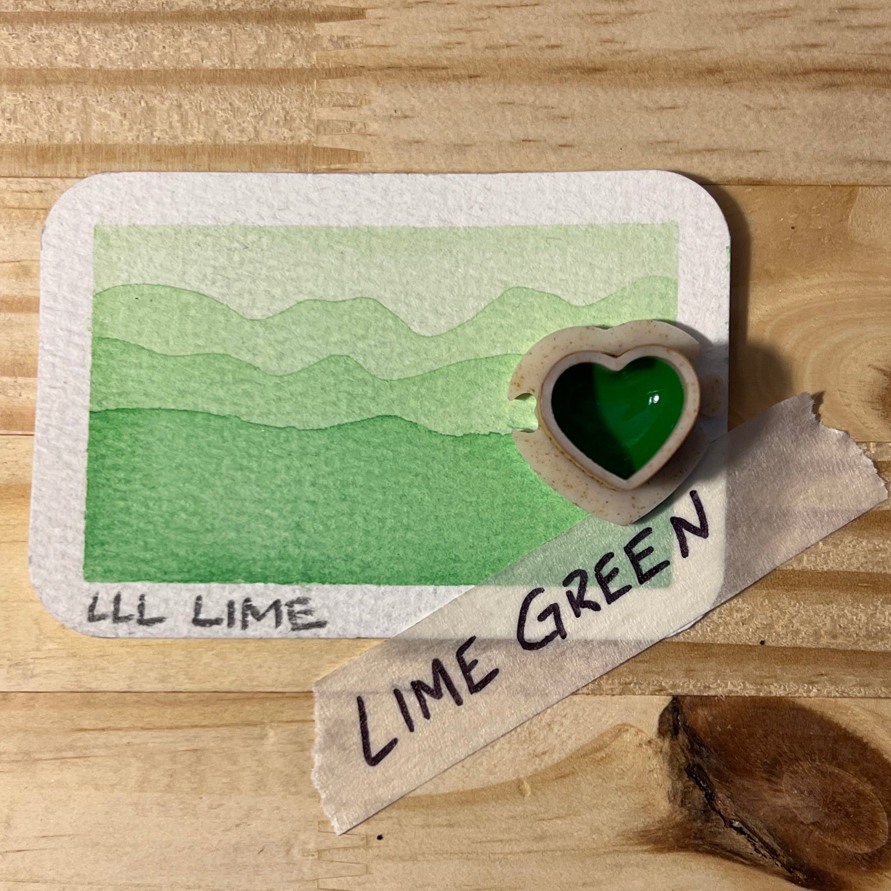 Lime green color swatch on a wooden surface with a heart-shaped half pan of paint and Lime green label.