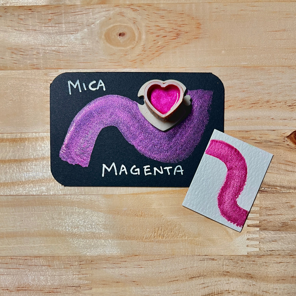 Magenta mica shimmer watercolor paint  heart shape paint pan with swatch on on a black card with 'Mica Magenta' text and small swatch on white paper