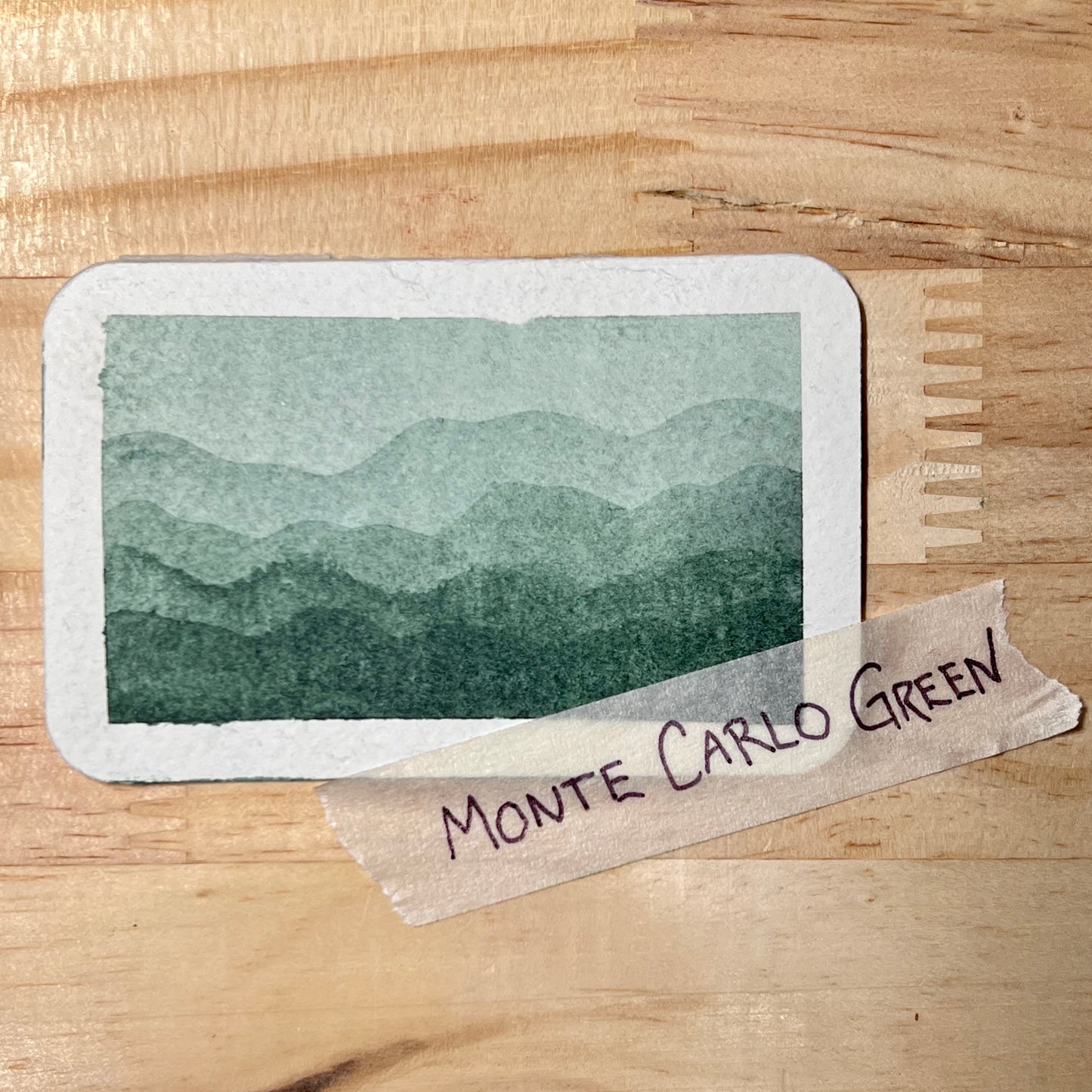 Card with a mountain landscape illustration and 'Monte Carlo Green' label on a wooden surface