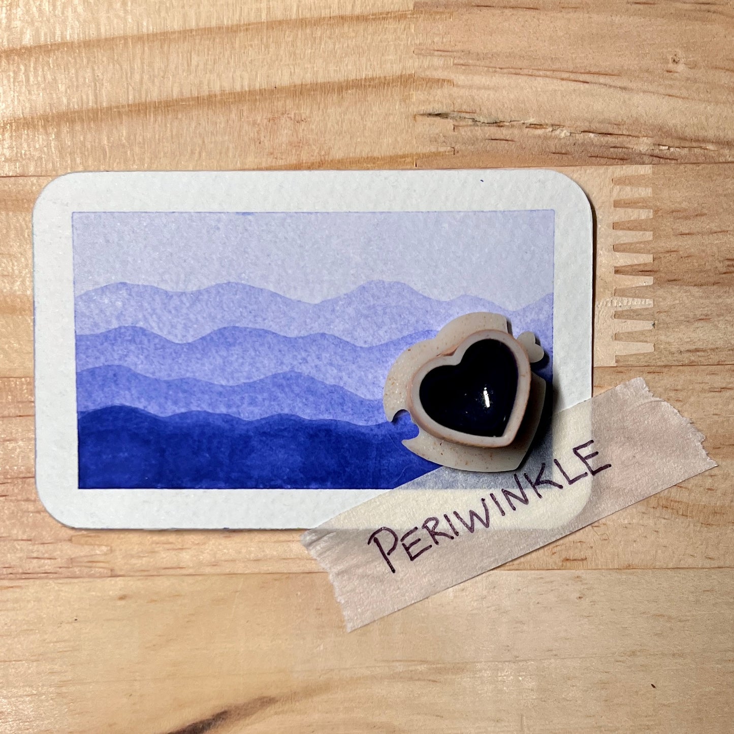 blue purple watercolor gradient landscape, heart-shape watercolor pan, labeled 'periwinkle', on a wooden surface.