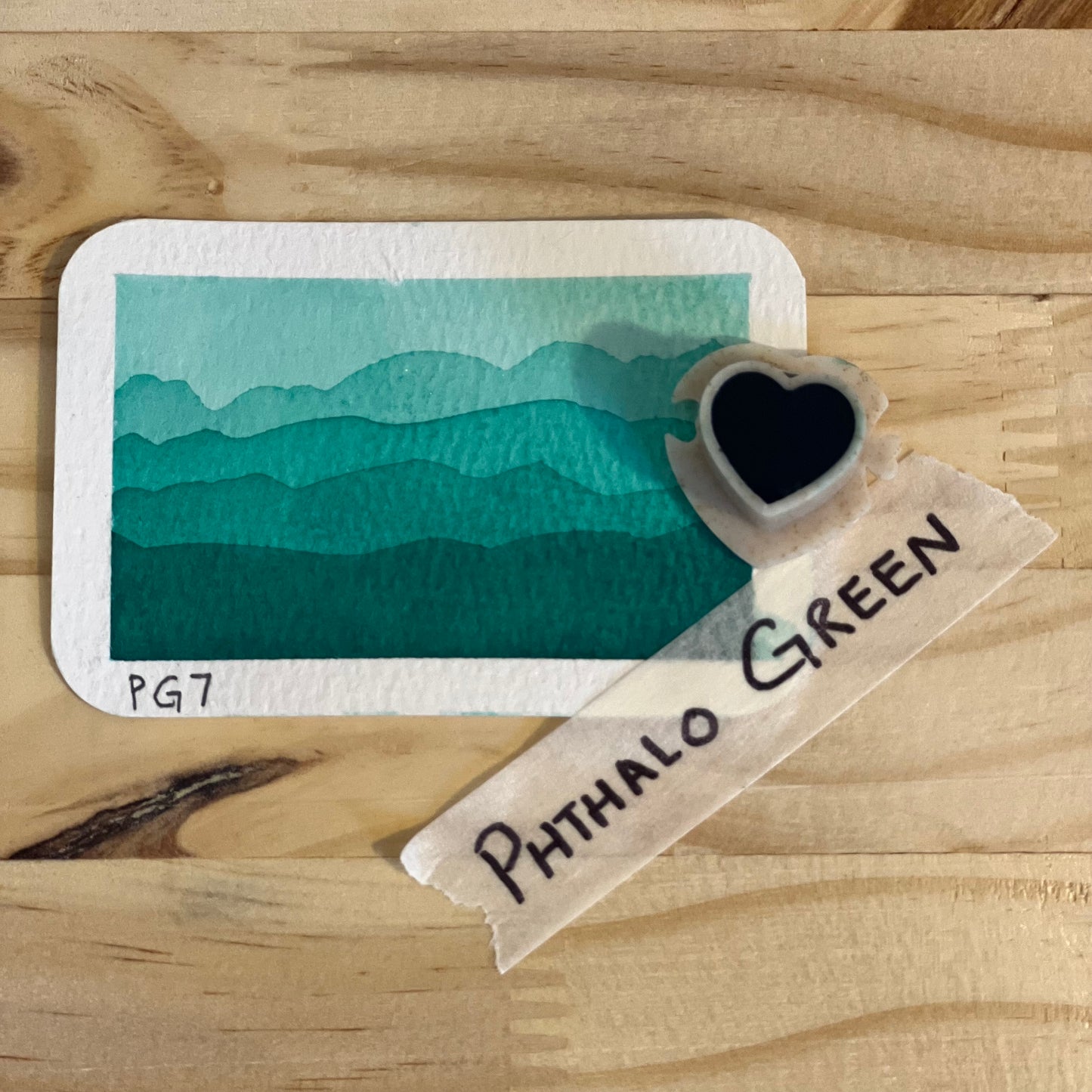 phthalo green watercolor gradient landscape, heart-shape watercolor pan, labeled 'Phthalo green', on a wooden surface.