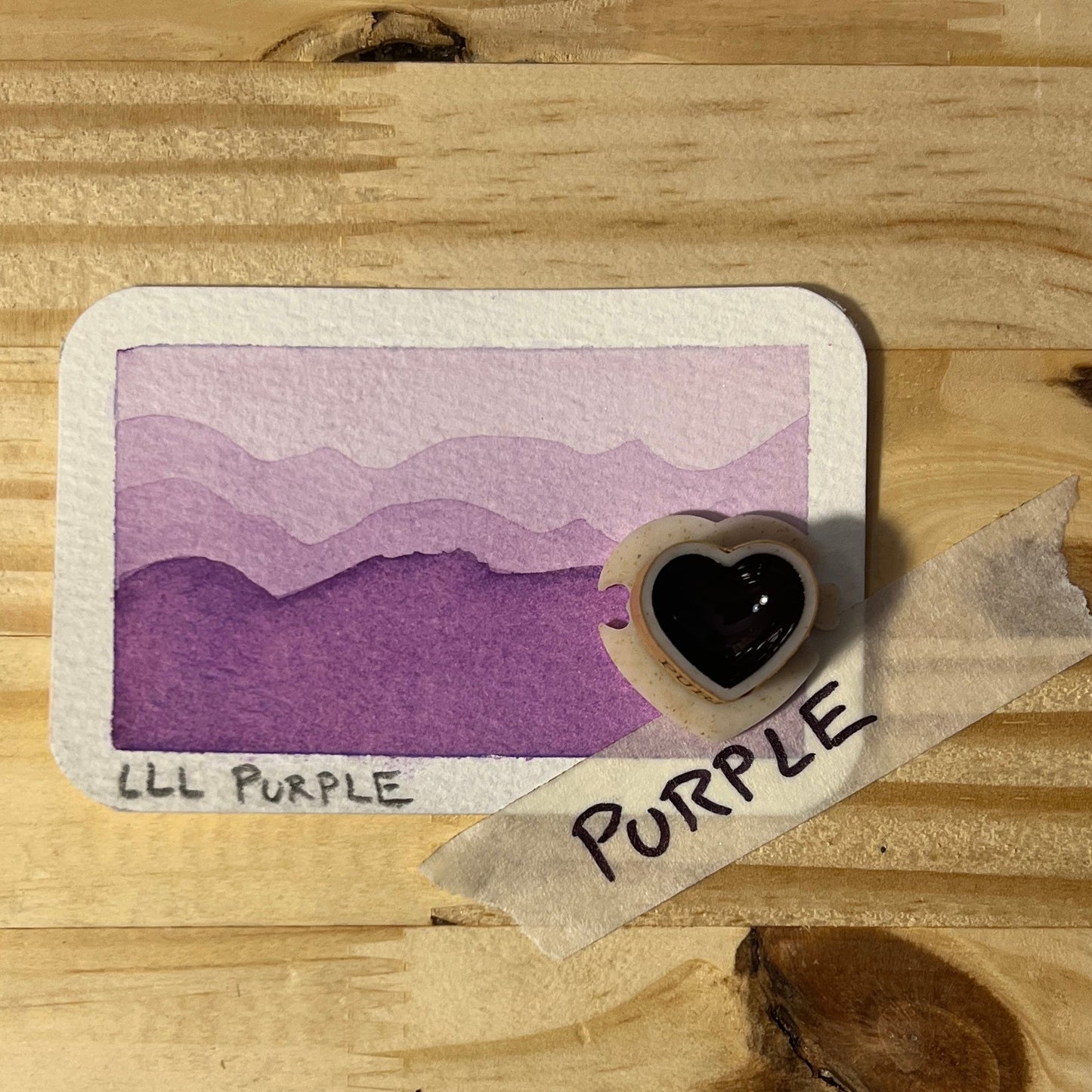 Card with purple color swatch and heart-shaped sticker on wooden surface