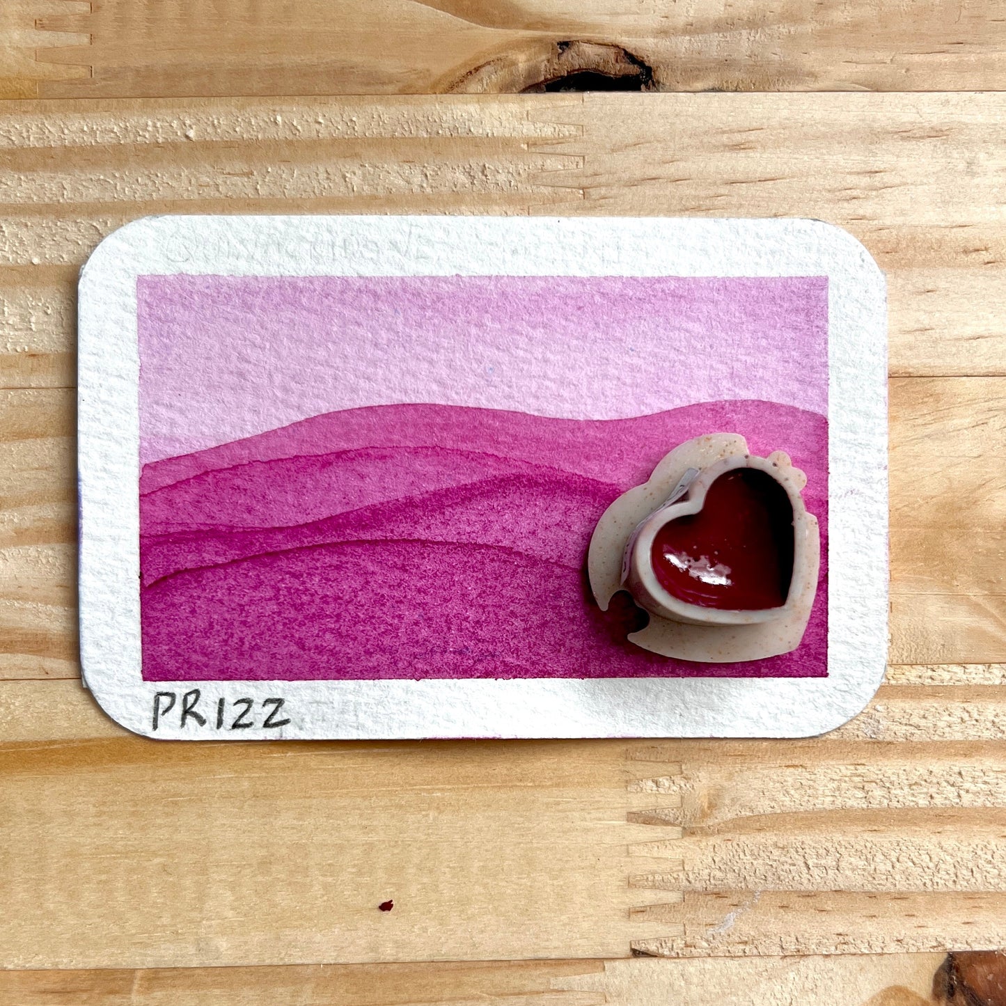 Card with a Magenta landscape and heart shaped pan of magenta paint on a wooden surface