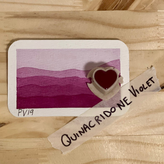 Violet watercolor gradient landscape, heart-shape watercolor pan, labeled 'quinacridone violet', on a wooden surface.
