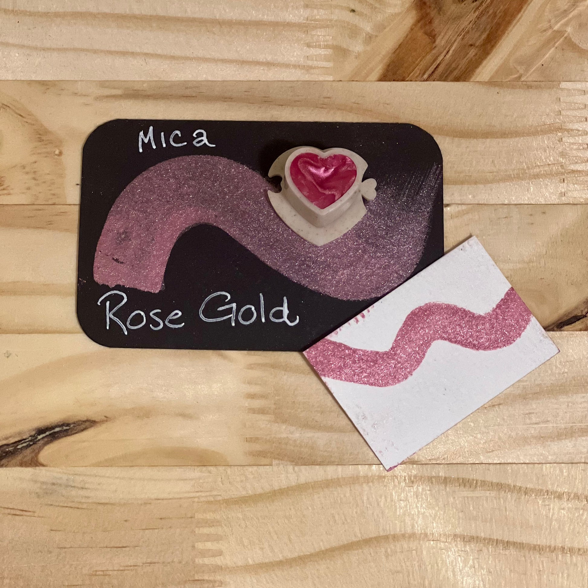Rose gold mica shimmer watercolor paint  heart shape paint pan with swatch on on a black card with 'Mica Rose Gold' text and small swatch on white paper
