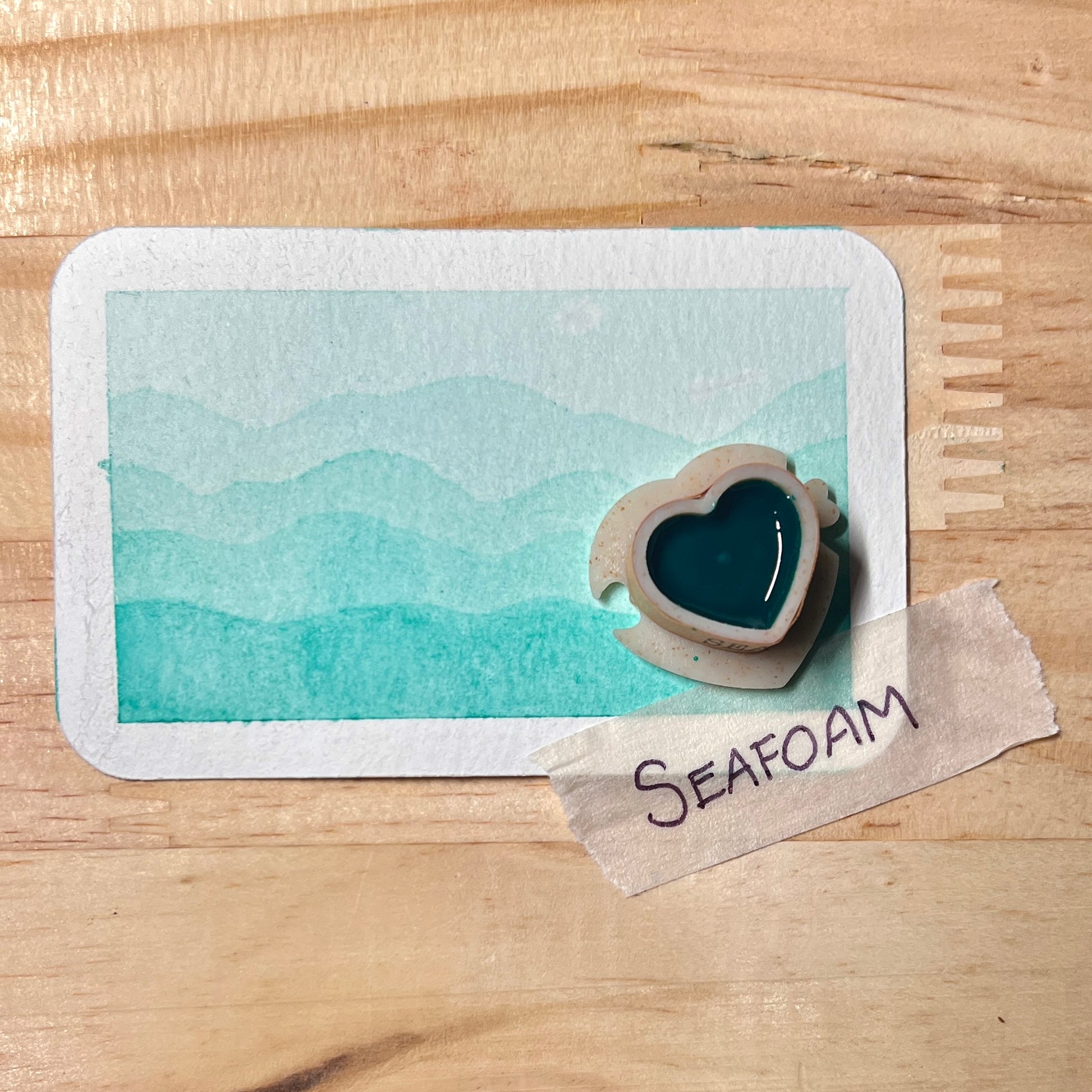 light Blue-green watercolor gradient landscape, heart-shape watercolor pan, labeled 'Seafoam', on a wooden surface.